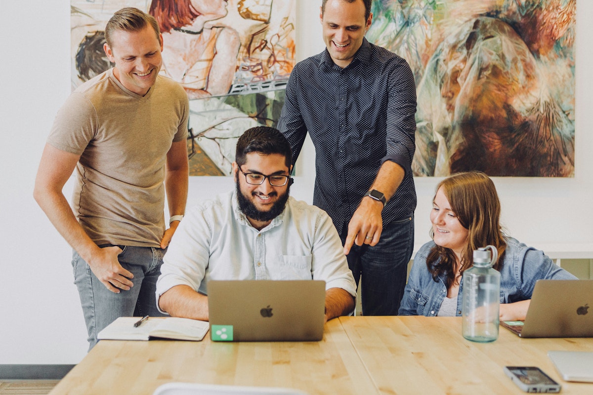 A group of colleagues gathered around a laptop in the office